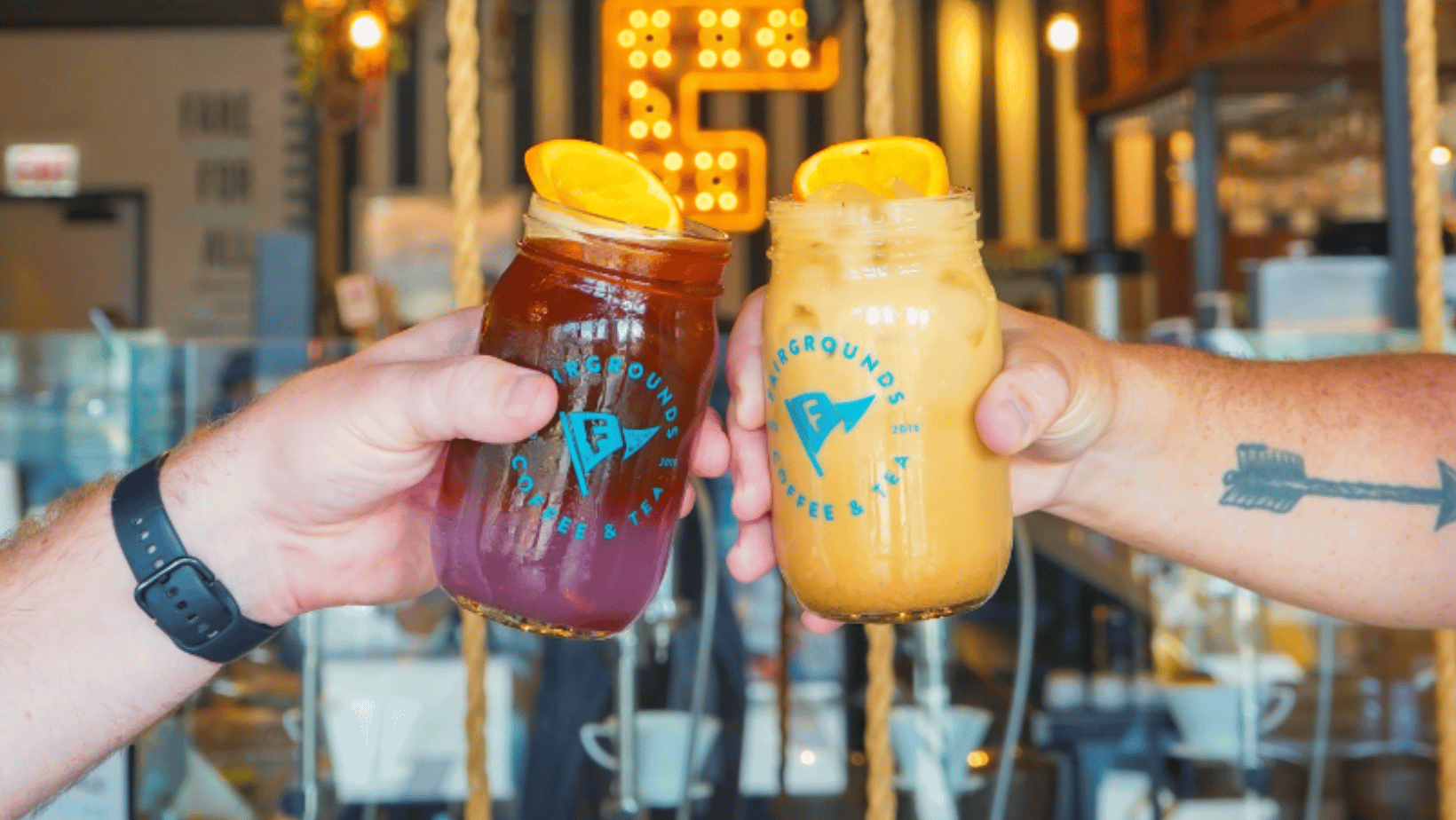 Two hands holding drinks from Fairgrounds craft coffee & tea 