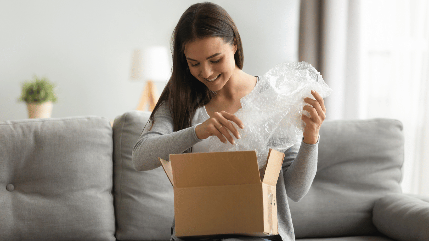 Young woman opening package on sofa